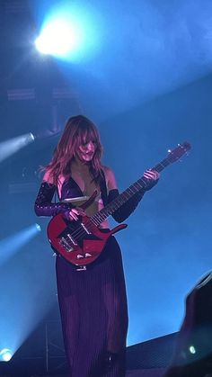 a woman in a long dress playing an electric guitar on stage with blue lights behind her