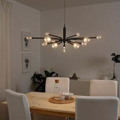 a dining room table with white chairs and lights hanging from it's center point