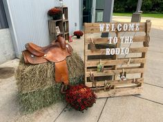 a wooden sign sitting next to a pile of hay with a saddle on top of it