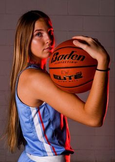 a woman holding a basketball in her right hand and looking at the camera with an intense look on her face