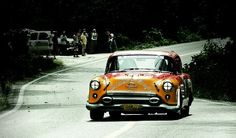 an orange and white car driving down a road with people standing on the side of it