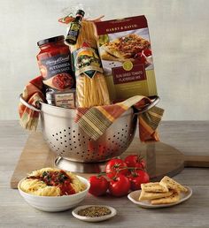 a large metal colander filled with pasta, tomatoes and other food items sitting on a wooden table