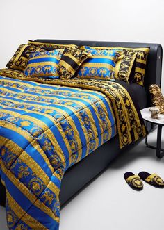 a bed with blue and gold bedspread next to two slippers on the floor