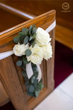 a bouquet of white roses and greenery is tied to the back of a church pew