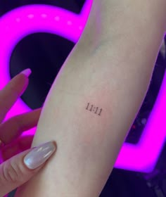 a woman's arm with the number 11 tattooed on her left arm, in front of a neon sign