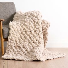 a white blanket sitting on top of a wooden floor next to a chair and wall