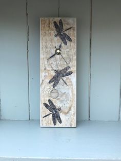 a wooden plaque with three dragonflies painted on it's sides, sitting on a shelf