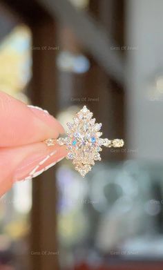 a woman's hand holding an engagement ring in front of her face, with the diamond