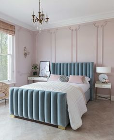 a bedroom with pink walls and blue velvet headboard, chandelier, bedding, and nightstands