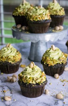 several cupcakes with green frosting and nuts on a marble table next to a cake plate