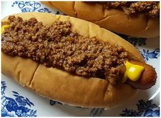 two hotdogs with chili and mustard sitting on a blue and white platter