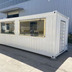 a white shipping container sitting in front of a building with windows on the side and doors open