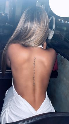 the back of a woman's neck with a tattoo on her lower back and words written in cursive writing