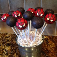 spiderman cake pops in a tin with shredded white paper on the top and black frosting on the bottom