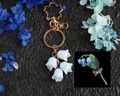 a blue flower is attached to a gold keychain with flowers in the background