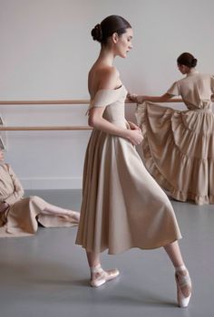 two ballerinas in beige dresses and one is sitting on the floor with her legs crossed