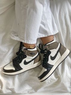 a person's feet with white and black sneakers on top of a bed covered in sheets