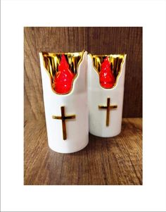 two white cups with red and gold designs on them, one has a cross in the middle