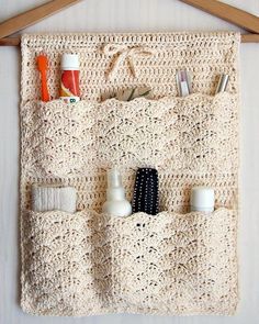 a crocheted purse hanging on a wall with toothbrushes and other items in it