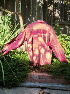 an orange and pink shirt sitting on top of a brick wall next to green plants