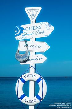 there are many signs on the pole by the water that say guess, beach club, and direction