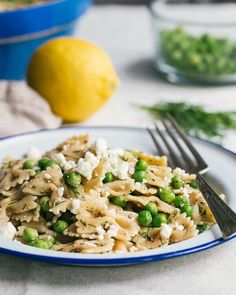 a white plate topped with pasta, peas and feta cheese next to a lemon