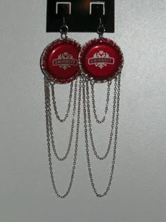 two red bottle caps with chains hanging from the wall next to a pair of earrings