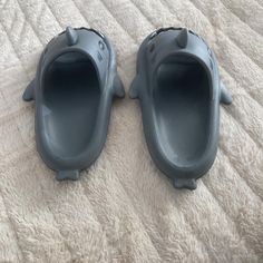 two gray plastic shoes laying on top of a bed next to each other with holes in them