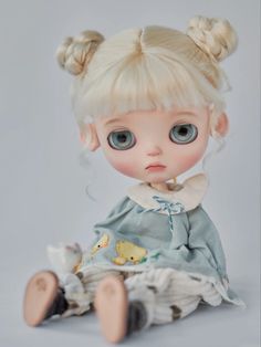 a doll with blonde hair and blue eyes sitting on top of a white floor wearing a dress