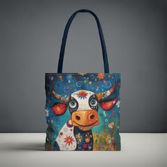 a cow painted on the side of a blue tote bag with flowers and stars