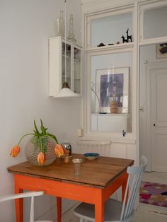 an orange table with two white chairs in front of it and a cabinet behind it