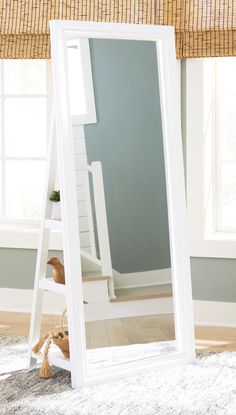 a large white mirror sitting on top of a wooden floor next to a window in a room