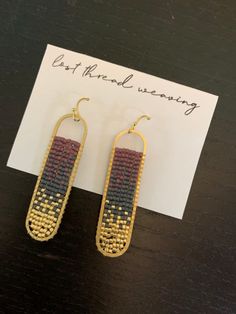 two pairs of earrings sitting on top of a table next to a piece of paper