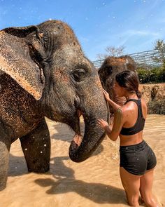 a woman is touching an elephant's face with her trunk in the water while it splashes