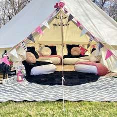 a tent that is set up in the grass with pillows and blankets on top of it