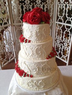 a three tiered wedding cake with red roses on the top and bottom, sitting on a table