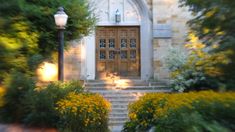 an old building with steps leading up to it and flowers in the foreground on either side