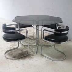 a glass table with four chairs and a black leather chair on the bottom one is in front of a white wall