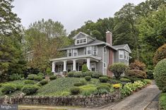 a gray house surrounded by lush green trees and shrubbery in front of the house