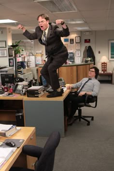 a man is standing on top of a desk in an office with his arms wide open