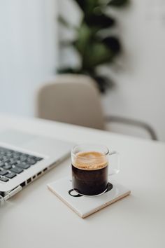 a cup of coffee sitting on top of a white plate next to a laptop computer