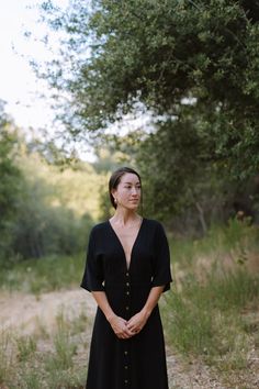 a woman standing in the middle of a field wearing a black dress with buttons on it