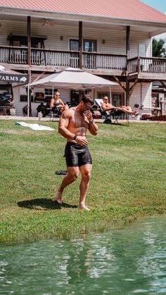 a shirtless man is playing frisbee in the grass next to a body of water