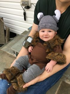 a man holding a baby wearing a knitted hat and furry bear mitt on his lap