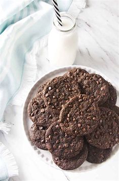 a white plate topped with chocolate cookies next to a glass of milk