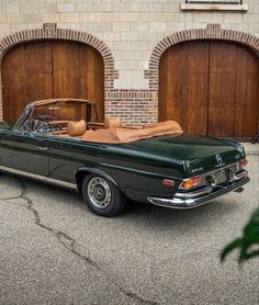 an old mercedes benz is parked in front of two garage doors with the top down