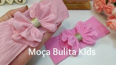 a hand holding two pink hair bows on top of a white table next to flowers