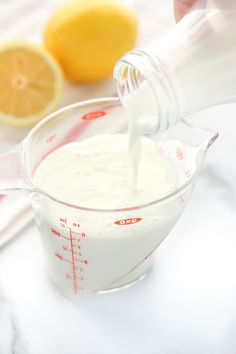 a person pouring milk into a glass measuring cup with lemons in the back ground