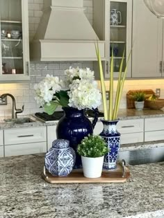 two vases with flowers are on a tray in the middle of a kitchen counter