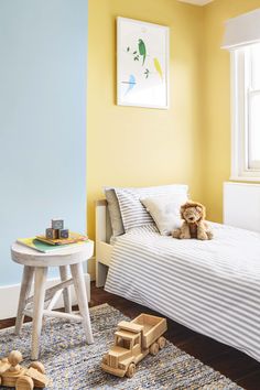 a small child's bedroom with yellow walls and white furniture, including a toy train on the floor